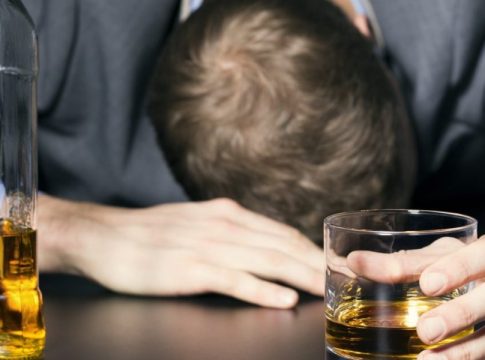 A man fell asleep next to a bottle with a glass in his hand